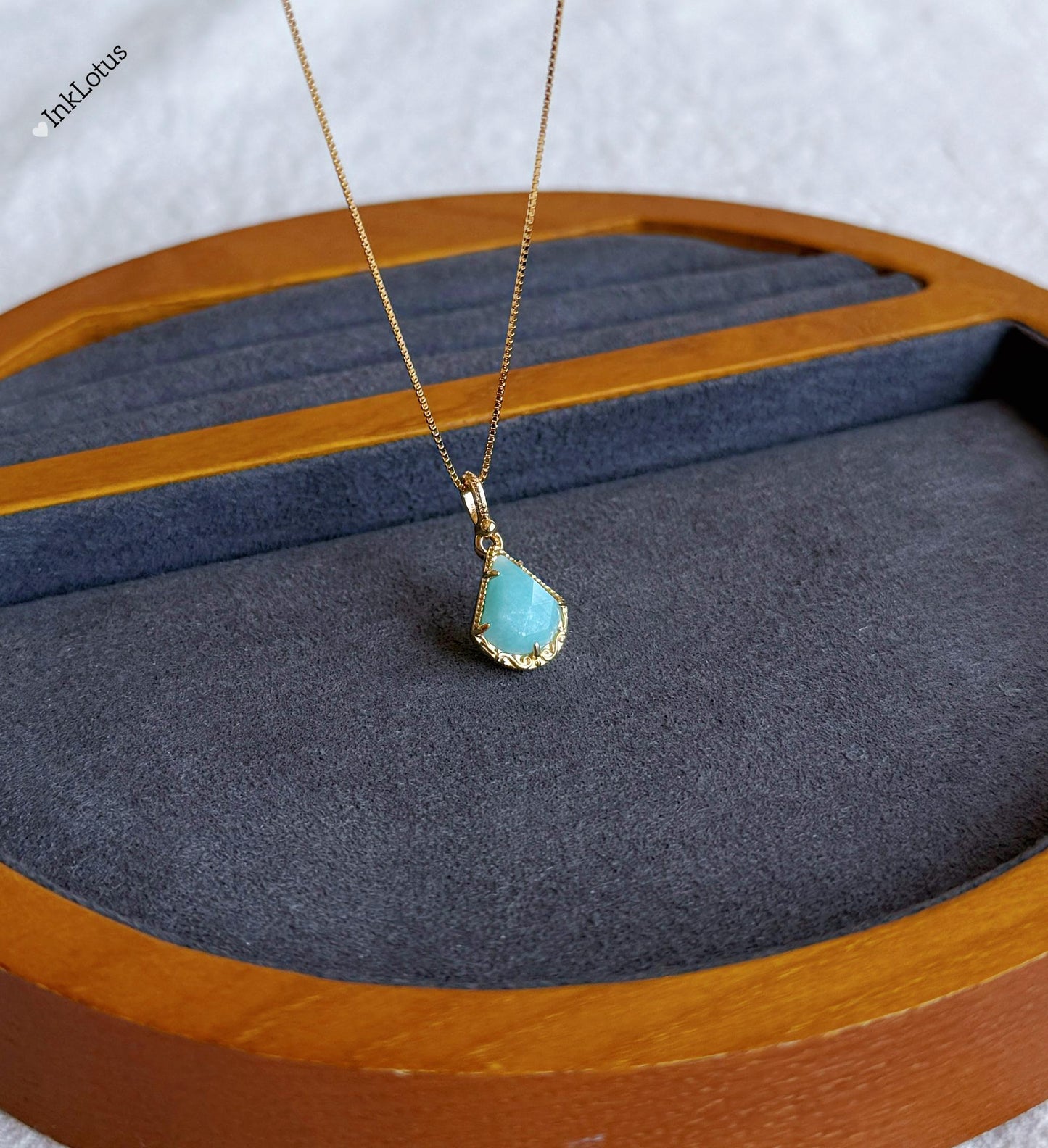 May include: A gold chain necklace with a teardrop-shaped pendant. The pendant is a light blue gemstone with a gold border.