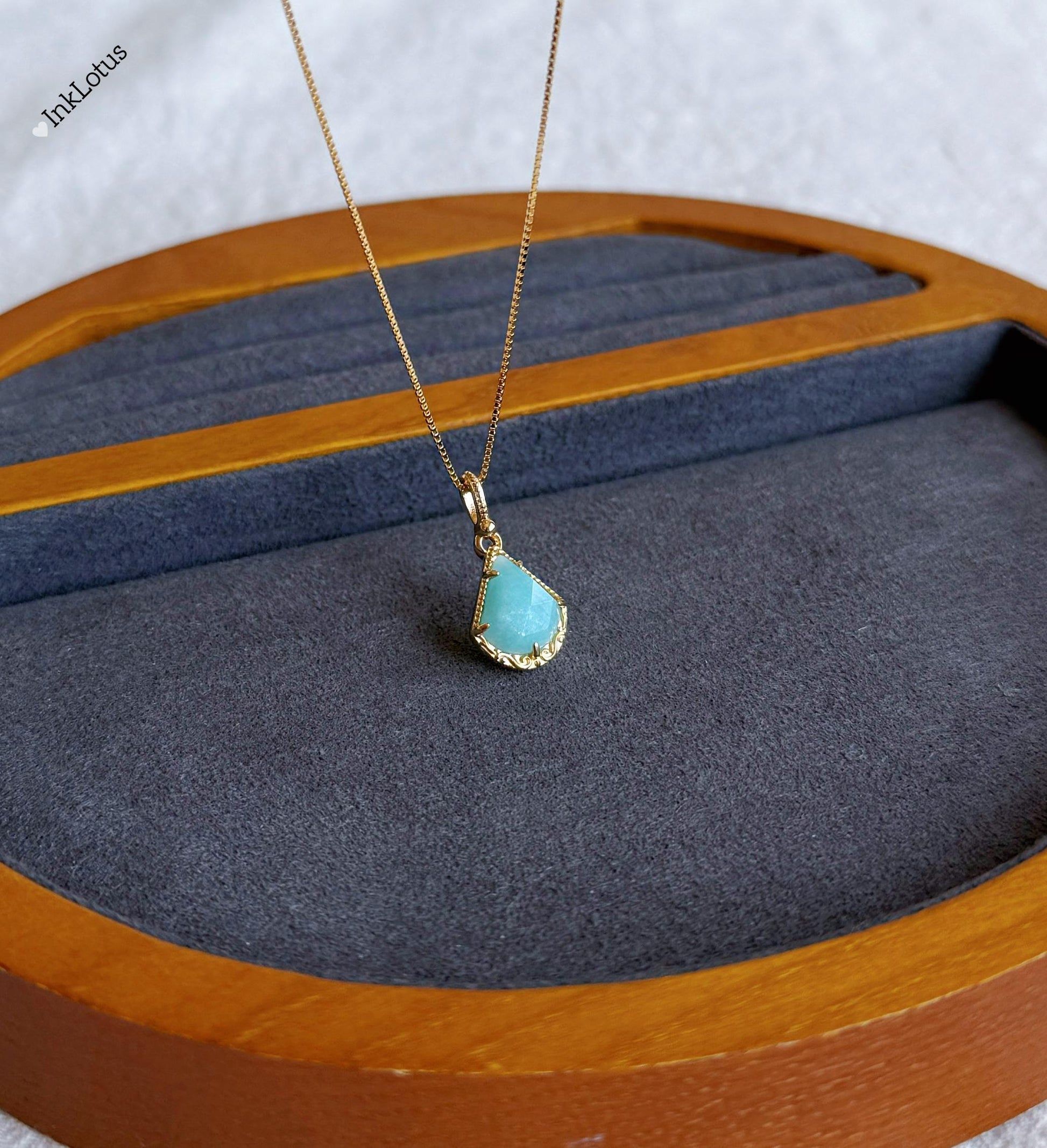 May include: A gold chain necklace with a teardrop-shaped pendant. The pendant is a light blue gemstone with a gold border.